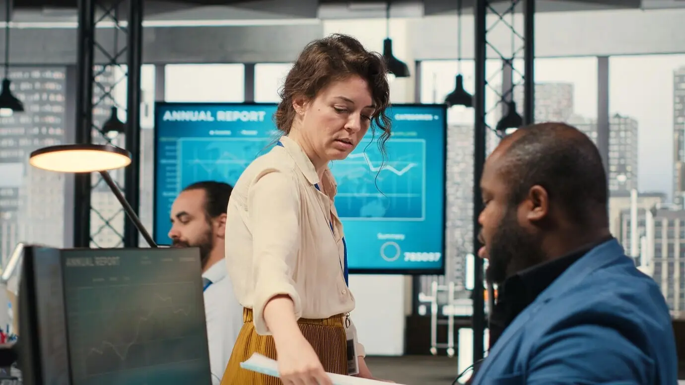 Женщина-секретарь в офисе толкает тележку, заполненную документами.